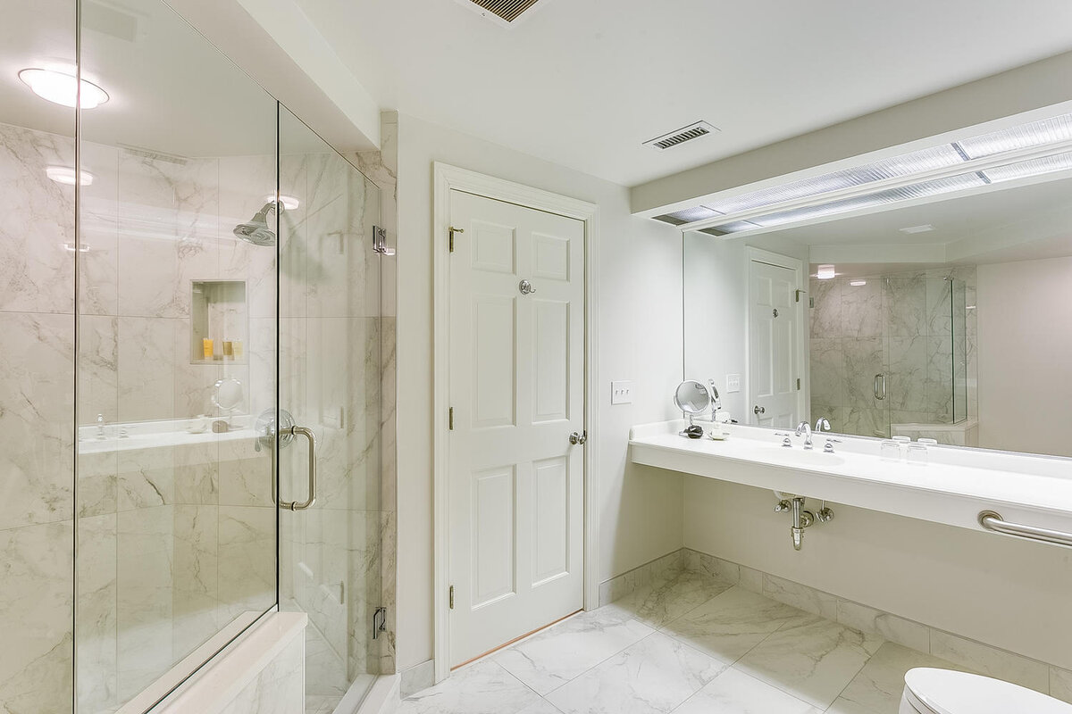 A modern bathroom with a glass-enclosed shower, marble tiles, a double sink, and a large mirror.