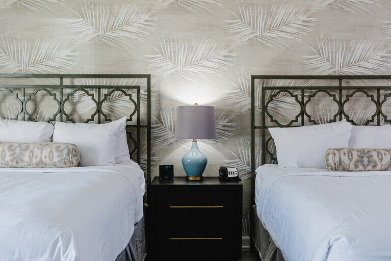 A neatly arranged hotel room with two beds, a nightstand, and a lamp.