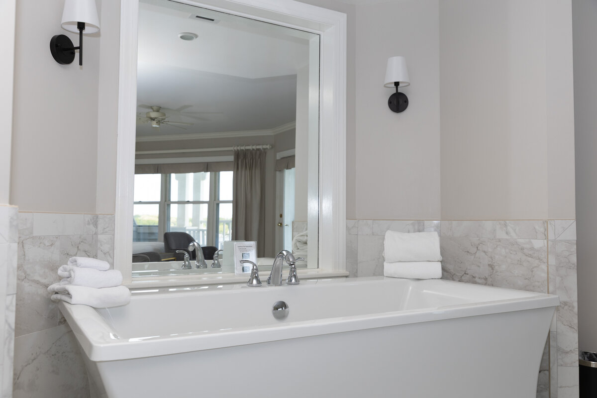 A clean and modern bathroom with a large soaking tub, marble tile, and a mirror.
