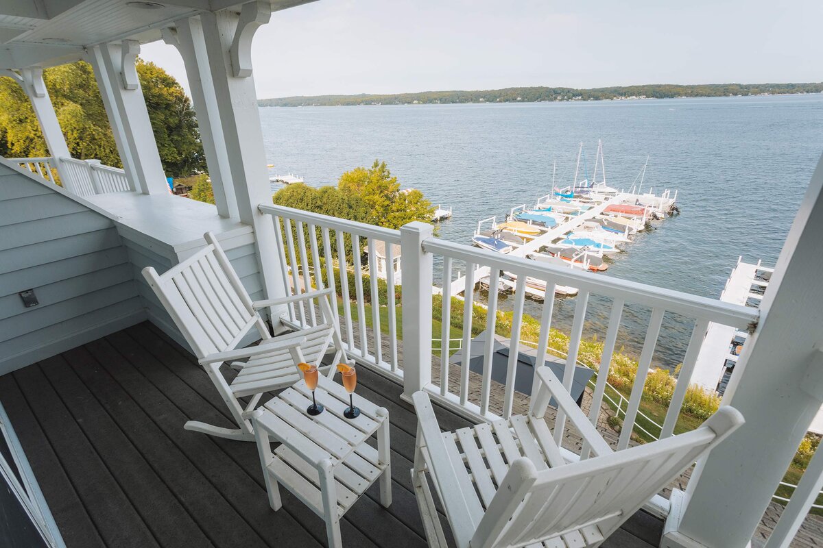 A lake view from a deck with white chairs and a railing.