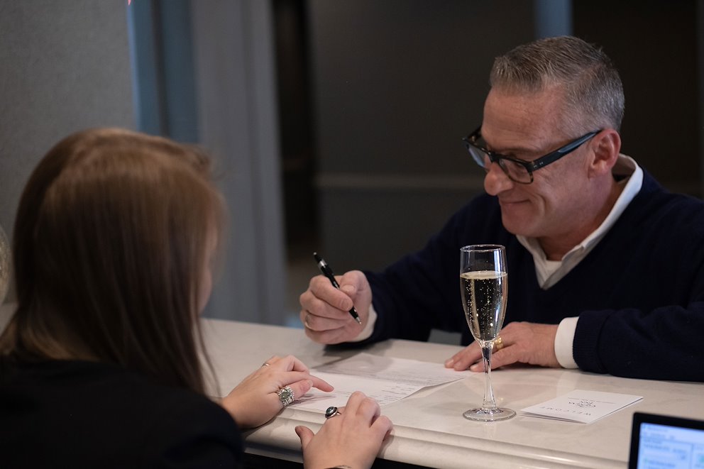 A man and woman at a reception desk with a champagne glass, engaged in a check-in process.