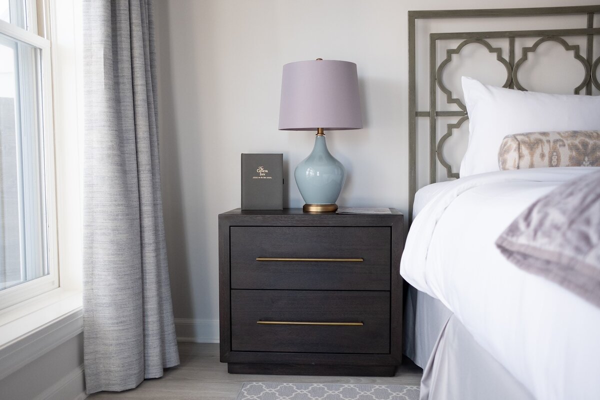 A neatly arranged guest room with a dark wood nightstand, blue lamp, and white bedding.