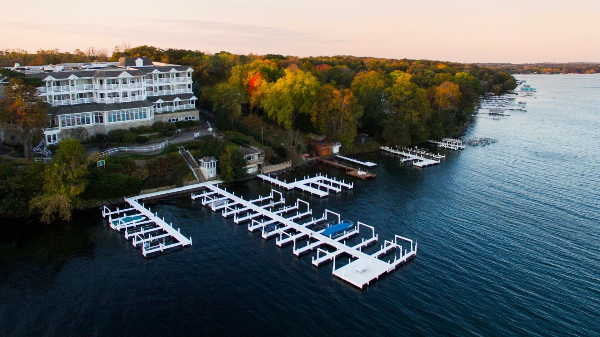 Aerial view of a large white hotel on the shore of a lake with docks and trees.